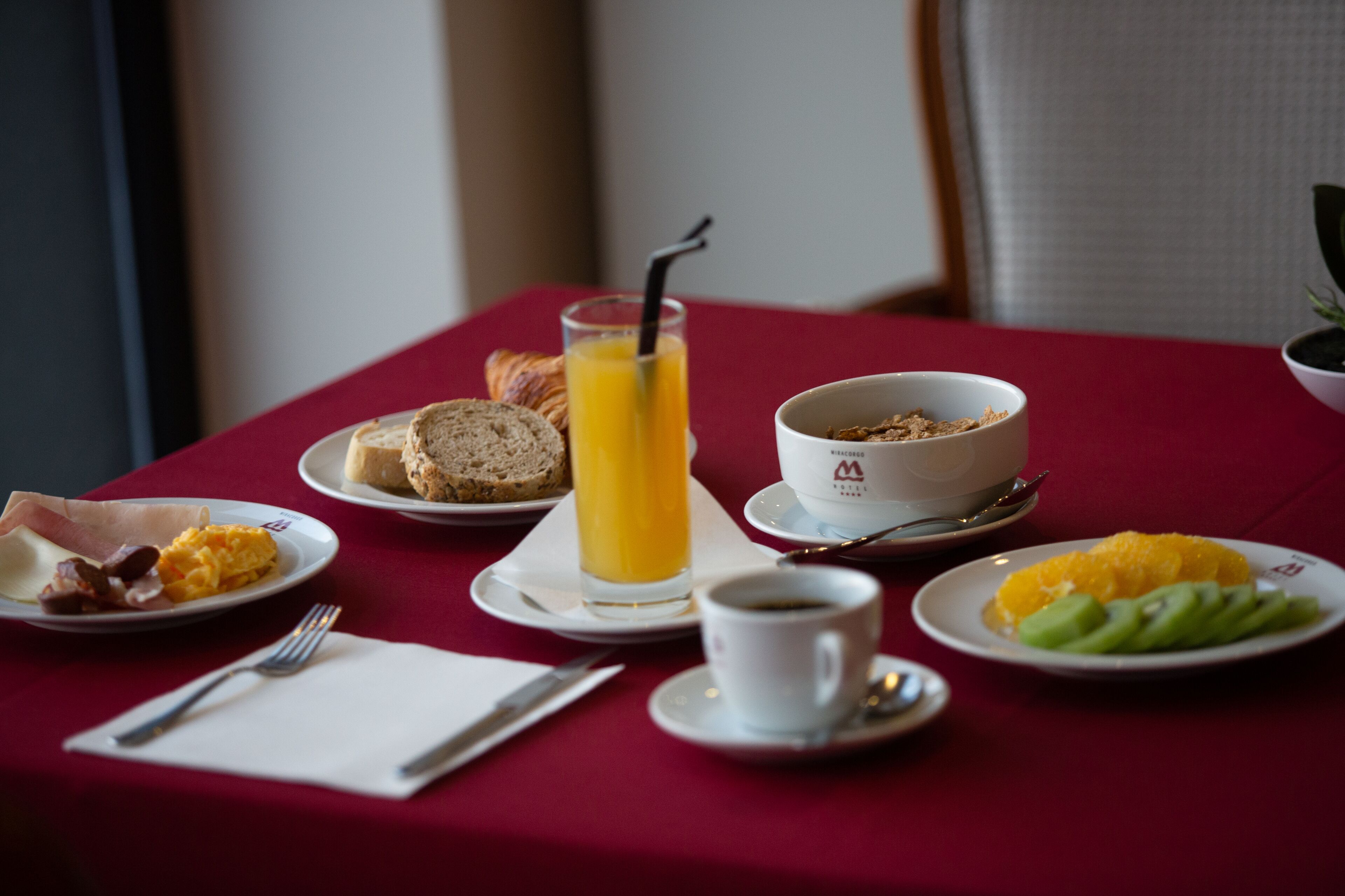 Een ontbijttafel met borden eten, een glas sinaasappelsap, een kom cornflakes en een kop koffie.
