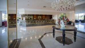 Un vestíbulo de hotel con una recepción, una araña y una mesa redonda con un jarrón de flores.