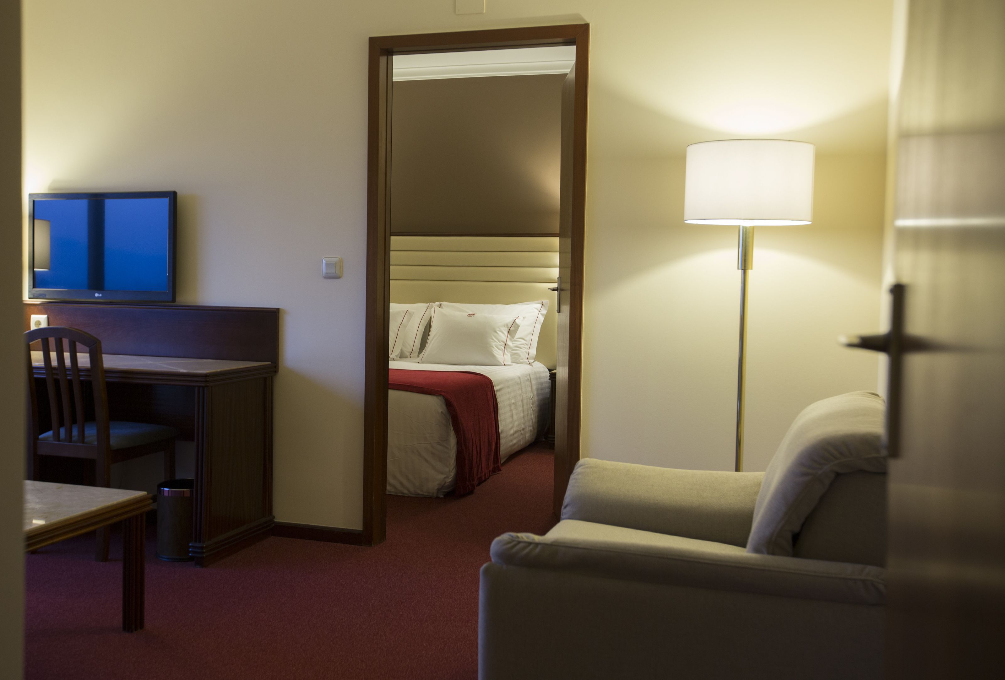 Een hotelkamer met een bureau, stoel, bed en een lamp.