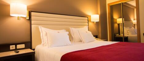 A hotel room with a large bed, two bedside lamps, a nightstand, and a mirror.