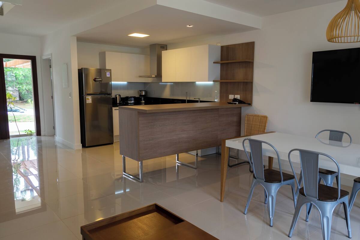 A modern kitchen with stainless steel appliances, a wooden island, and a dining area with metal chairs.