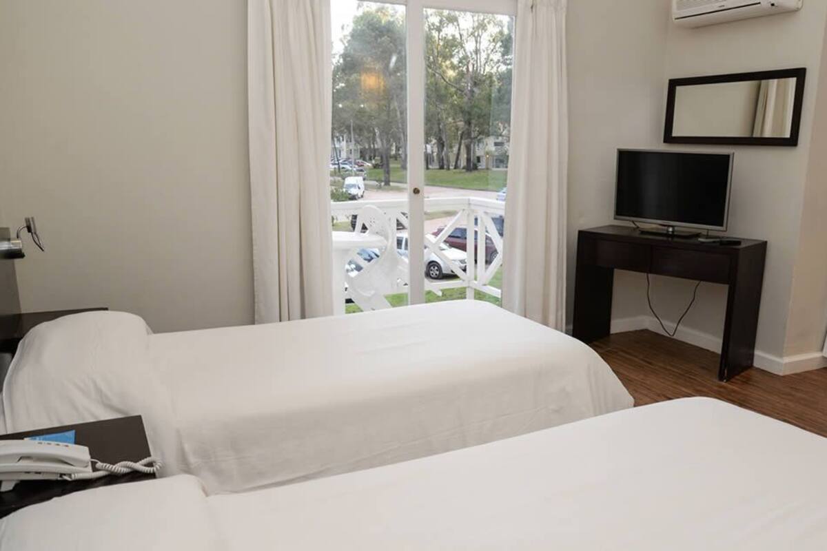 A hotel room with two beds, a TV, a desk, and a view of the street.