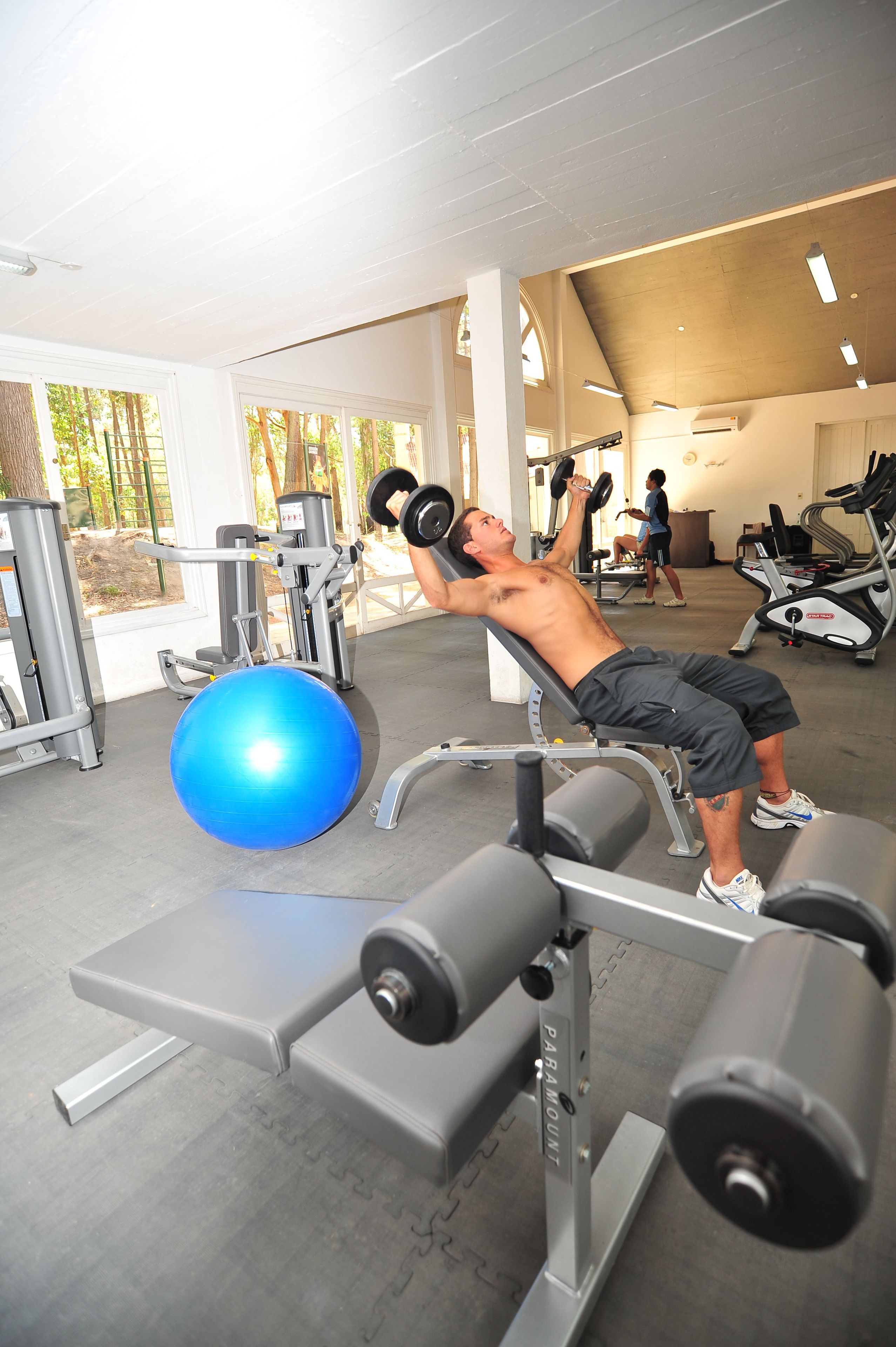 Een sportschool met fitnessapparatuur, een blauwe fitnessbal en een persoon die gewichten optilt.