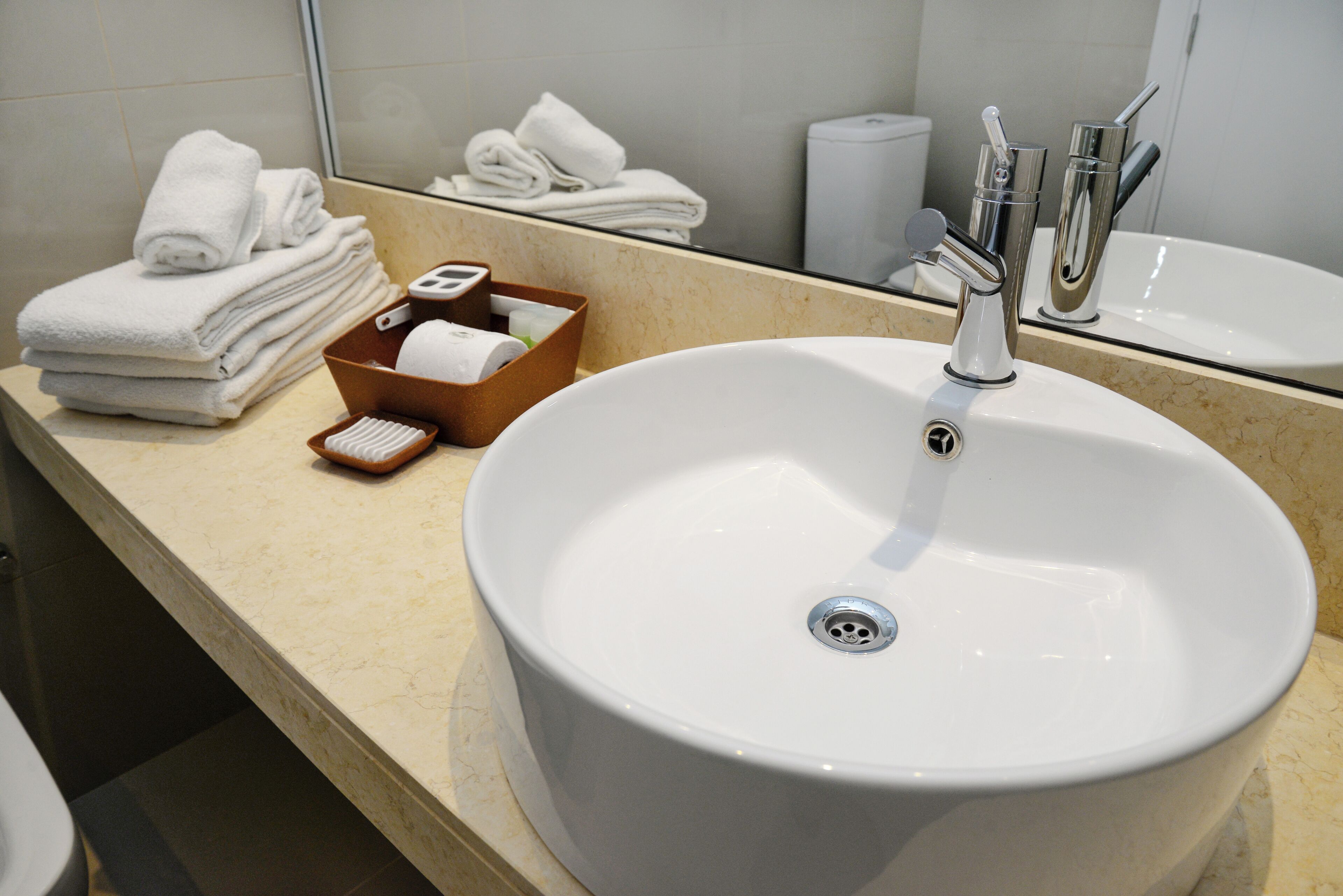 A bathroom with a large white sink, a mirror, and neatly stacked towels.