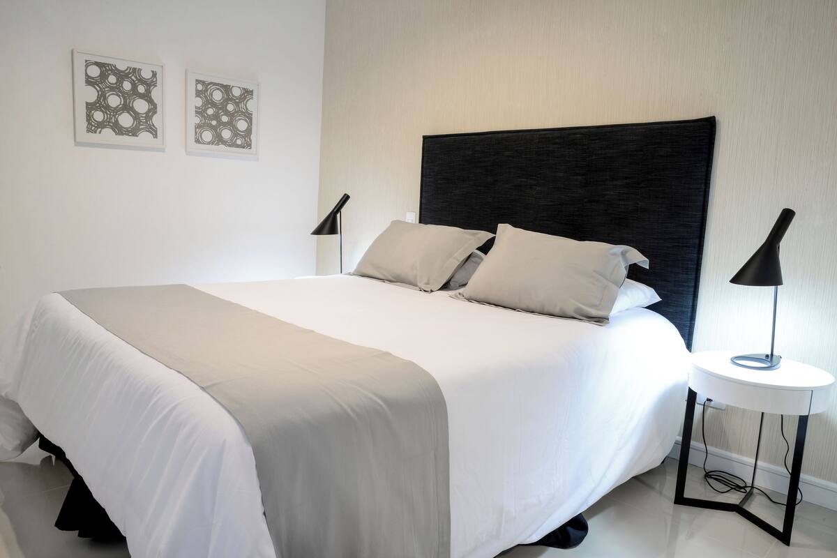 A neatly made bed with a dark headboard, two bedside lamps, and two framed wall art pieces.