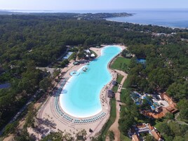 Vista aérea de un resort con una amplia piscina curva, rodeada de zonas de playa con sombrillas y tumbonas.