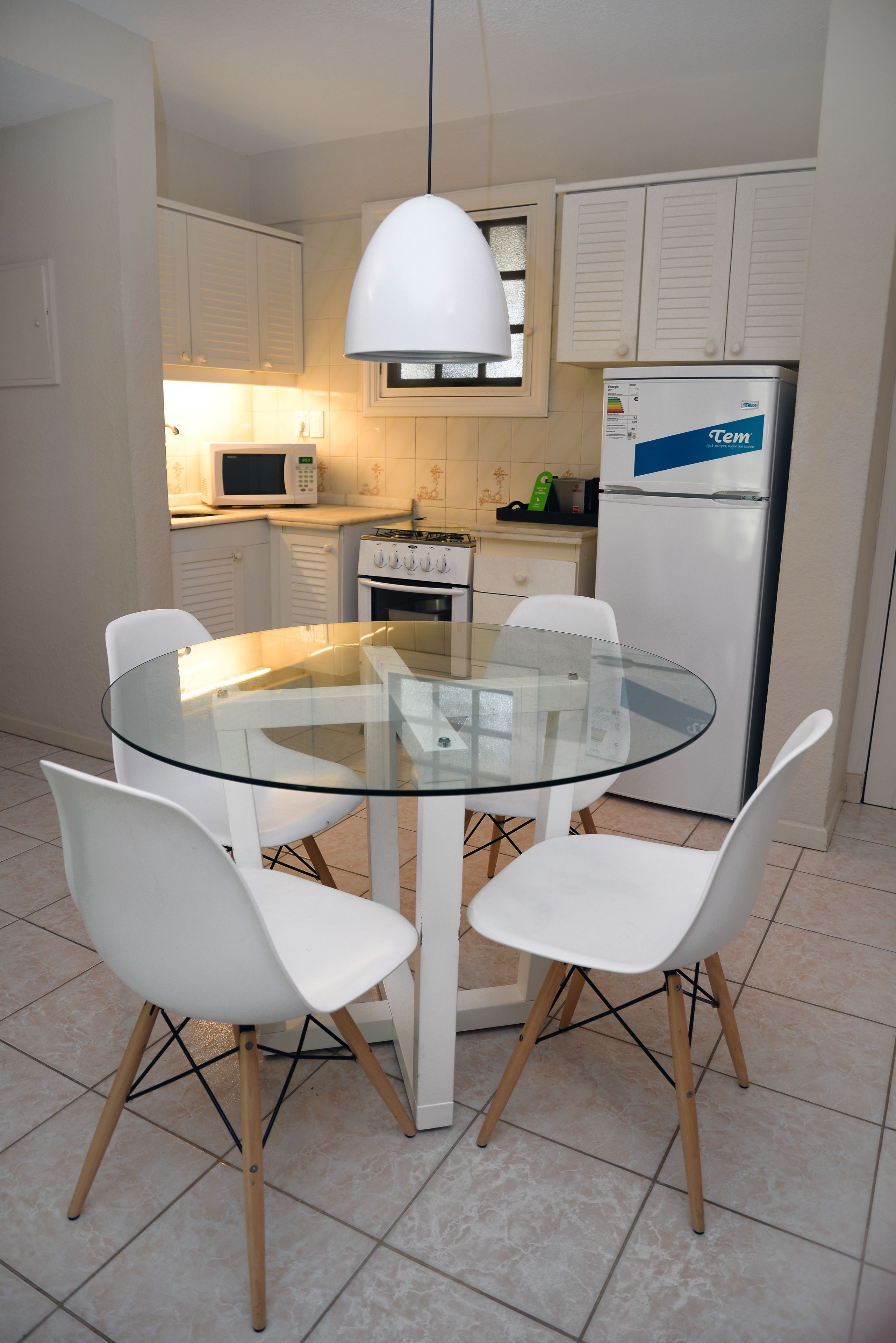 A modern kitchen with white cabinets, a glass-top dining table, and white chairs.