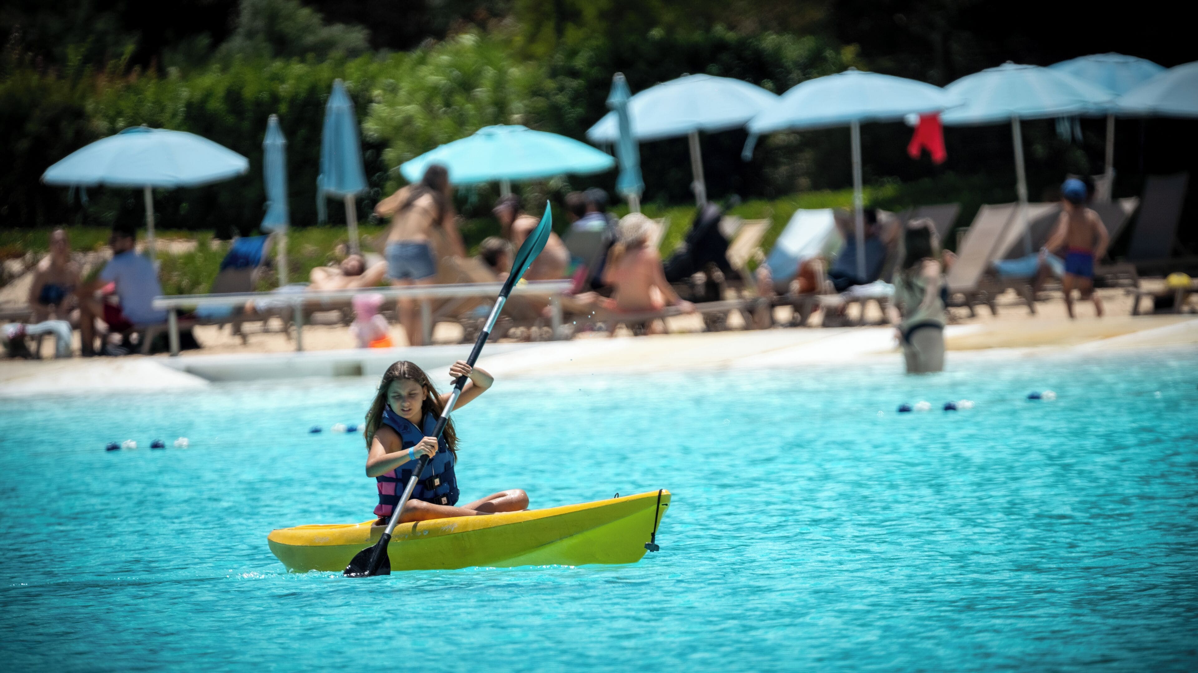 A person kayaking in a pool with lounge chairs and umbrellas in the background.