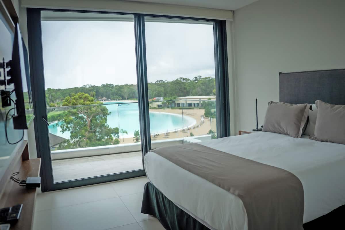 A hotel room with a large bed, a TV, and a view of a beach and pool.