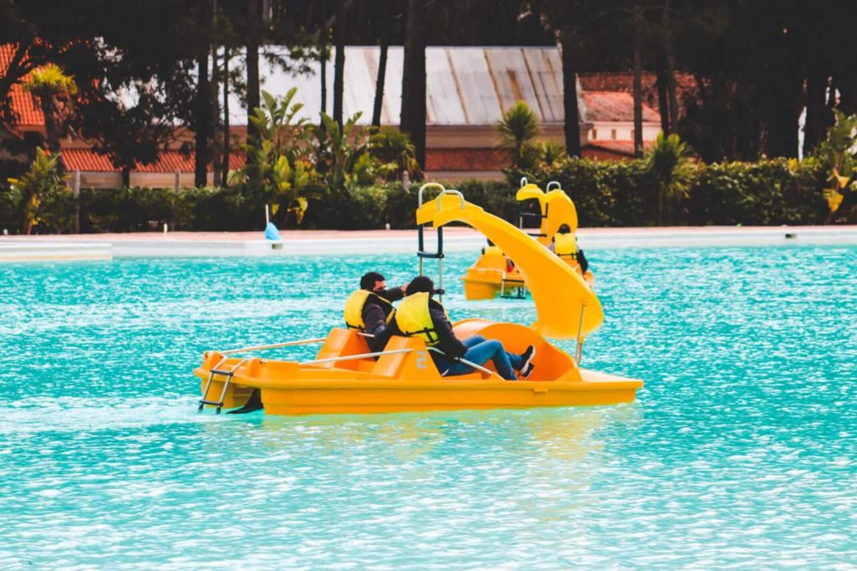 Ein Schwimmbecken mit gelben Tretbooten und Personen in Schwimmwesten.