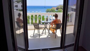 A balcony with a table and chairs, overlooking a coastal view with the sea and a hilly landscape. - Tony's Beach (Leros)