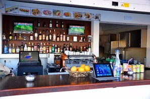 A bar area with a variety of liquor bottles, a laptop, a coffee machine, and a bowl of oranges on the counter.