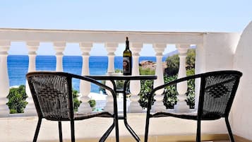 A balcony with a table and two wicker chairs, overlooking the sea.