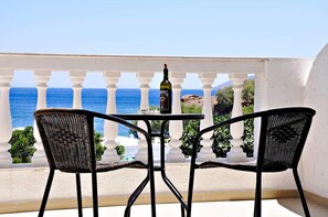A balcony with a table and two wicker chairs, overlooking the sea.