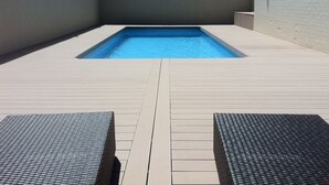 Una piscina al aire libre, sombrillas, sillones reclinables de piscina