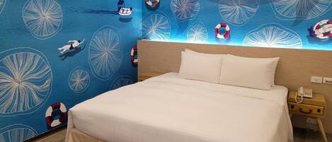 A hotel room with a bed, a nightstand, and a wall with a blue ocean-themed wallpaper.