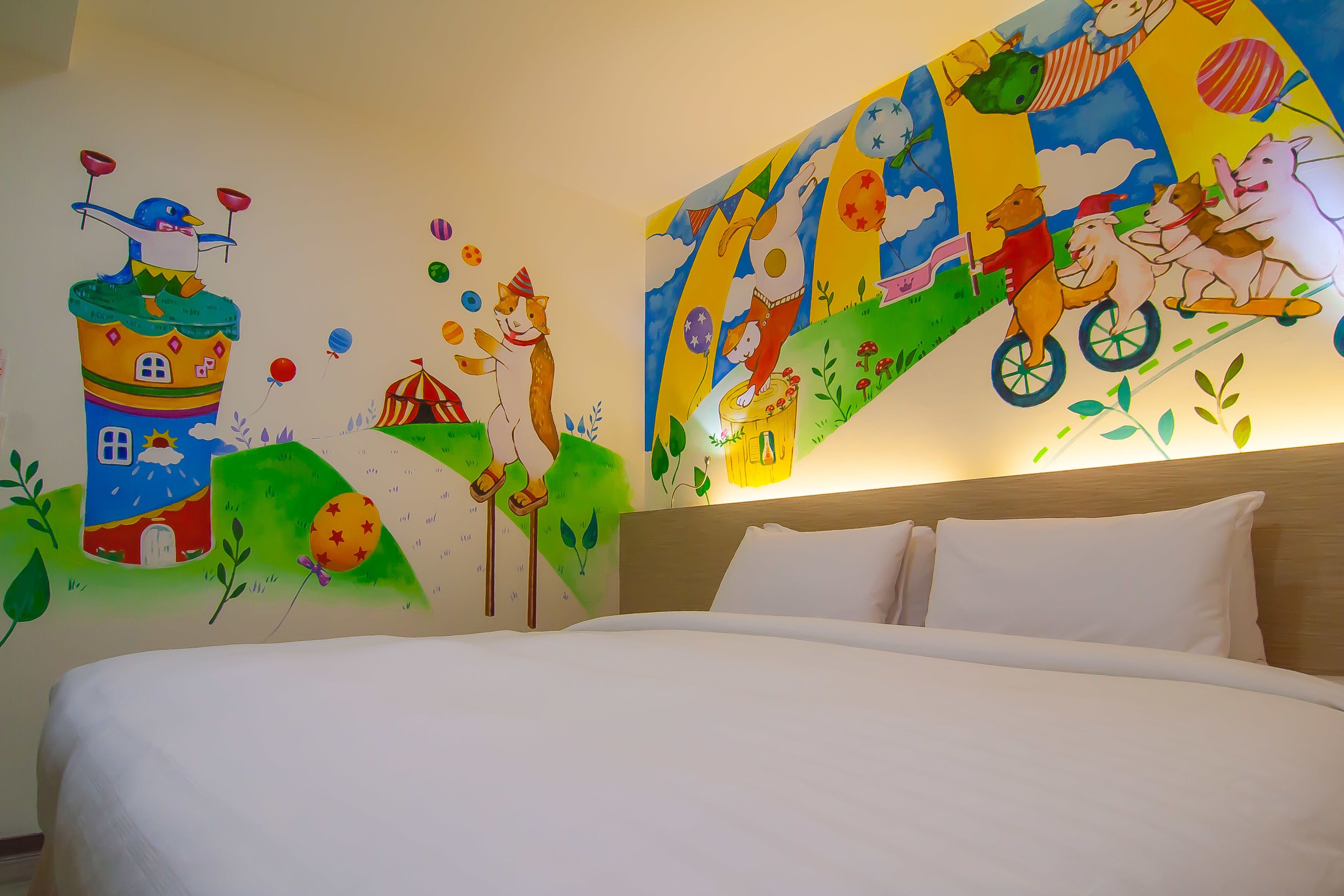 A hotel room with a large bed, a wooden headboard, and colorful wall art depicting animals and a house.