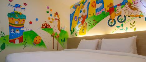 A hotel room with a large bed, a wooden headboard, and colorful wall art depicting animals and a house.