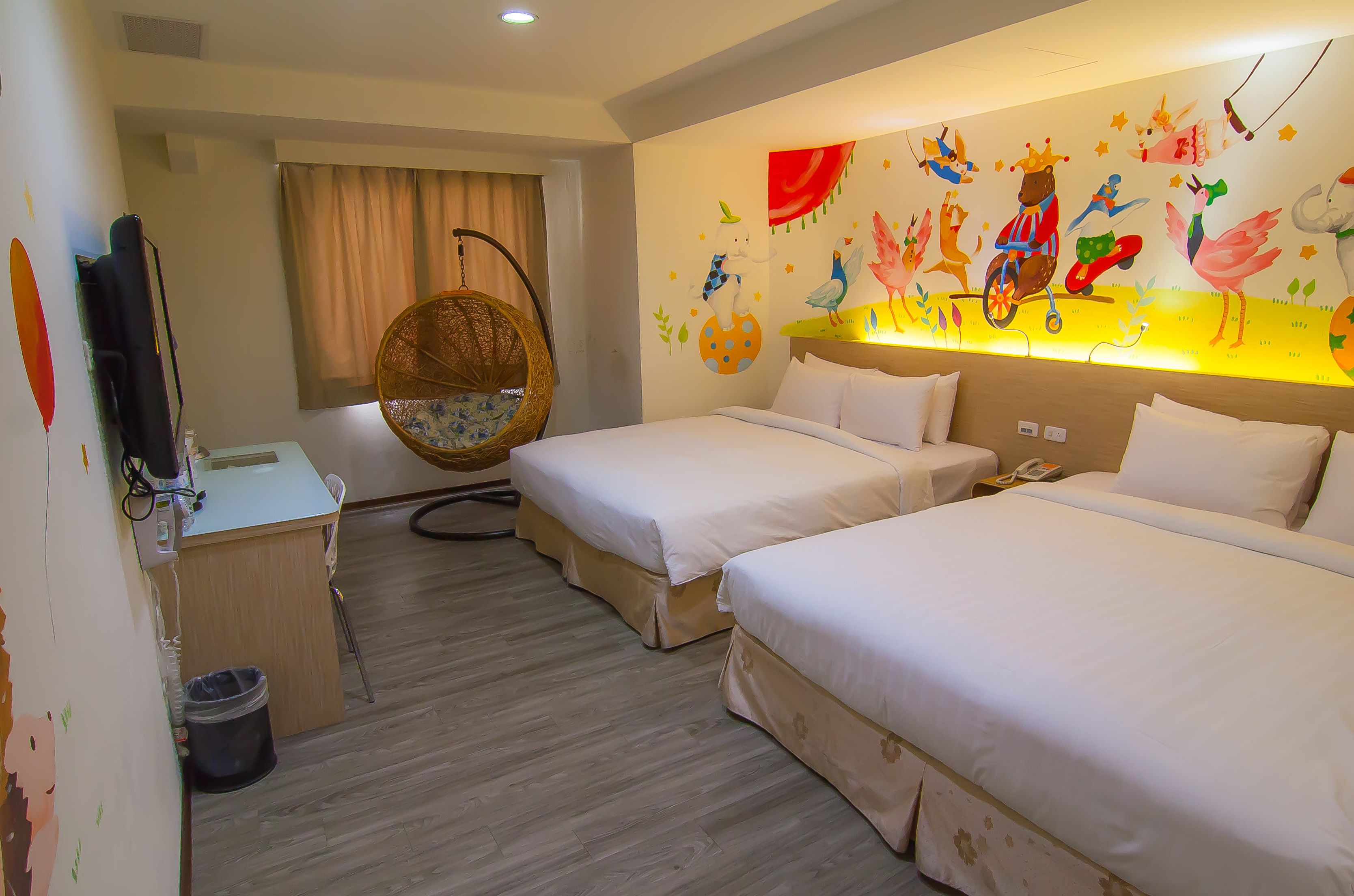 A hotel room with two beds, a desk with a chair, a hanging chair, and a wall mural.