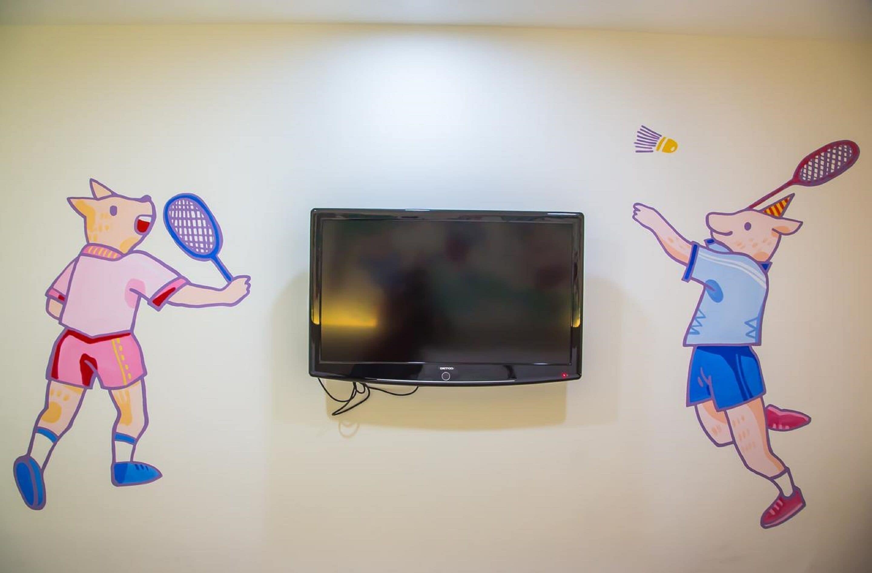 Un téléviseur à écran plat fixé au mur, avec deux personnages de dessins animés tenant des raquettes de tennis.