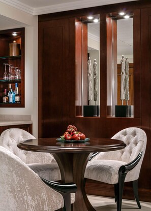 A dining area with a round table, two upholstered chairs, a fruit centerpiece, and a wooden cabinet with shelves. - One & Only Royal Mirage (Dubai)