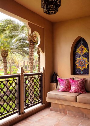 A balcony with a view of palm trees, a patterned wall, and a cushioned seating area with decorative pillows. - One & Only Royal Mirage (Dubai)