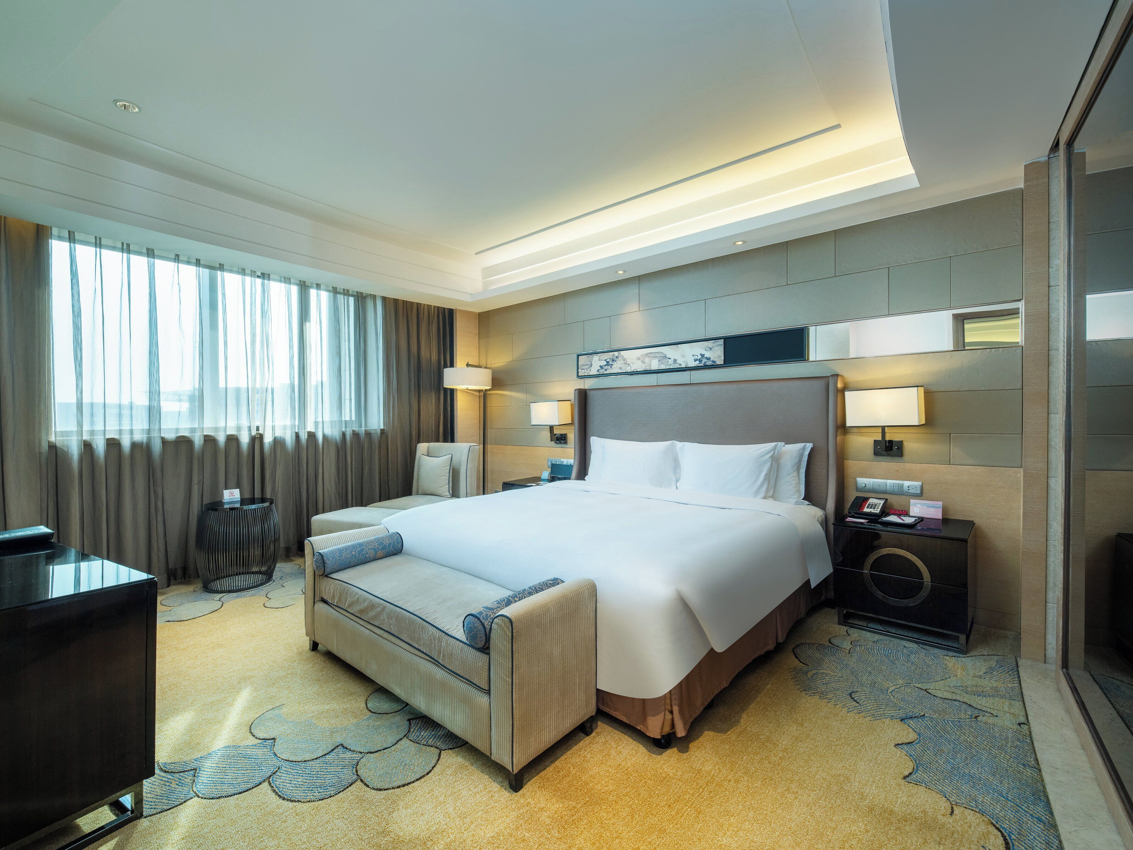 Une chambre d’hôtel moderne avec un grand lit, des tables de chevet, un bureau et une vue sur la ville.