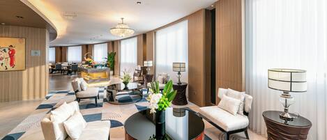 A spacious hotel lobby with a round coffee table, seating area, and a reception desk.