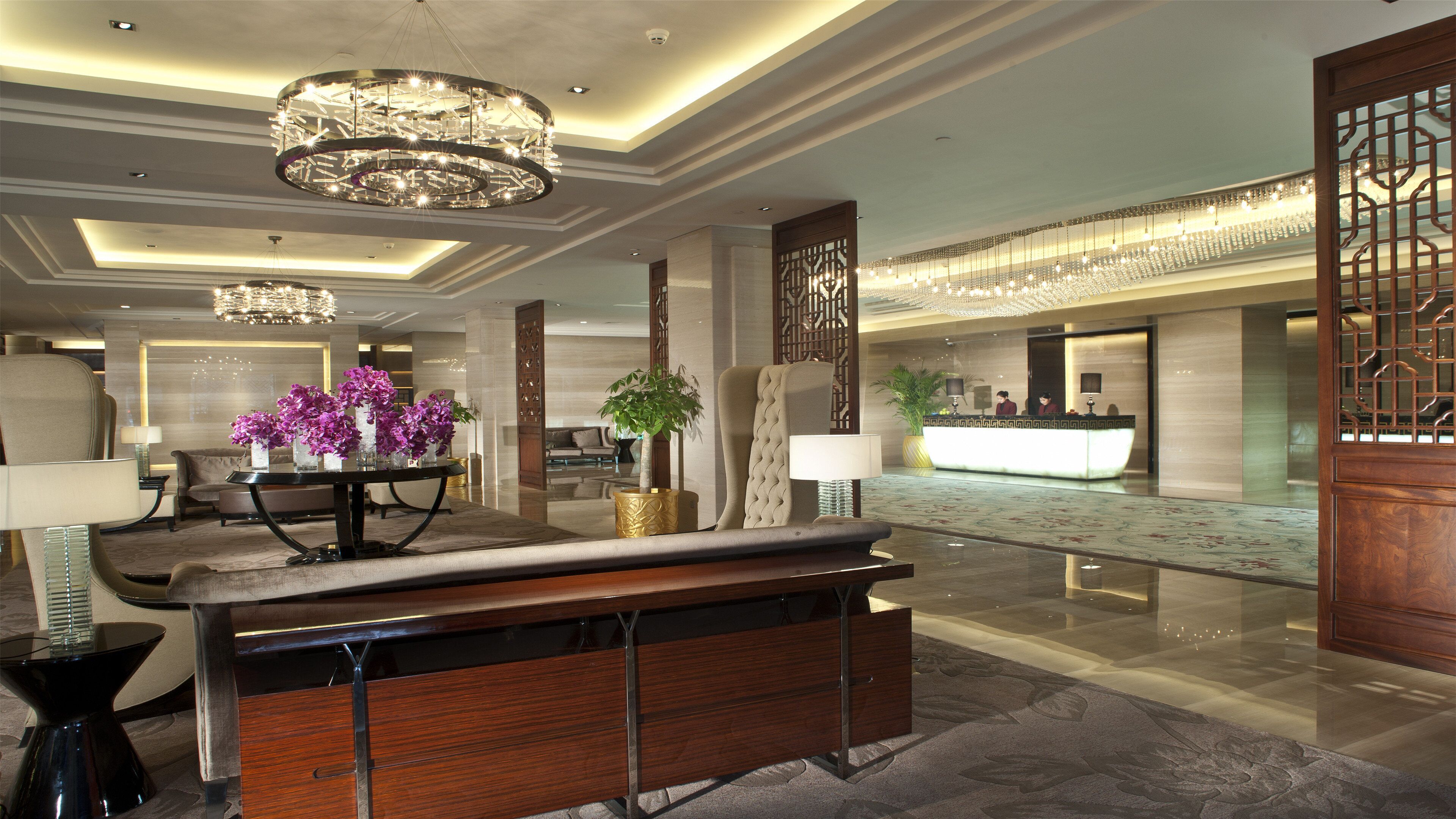 A hotel lobby with a reception desk, seating area, and a chandelier.