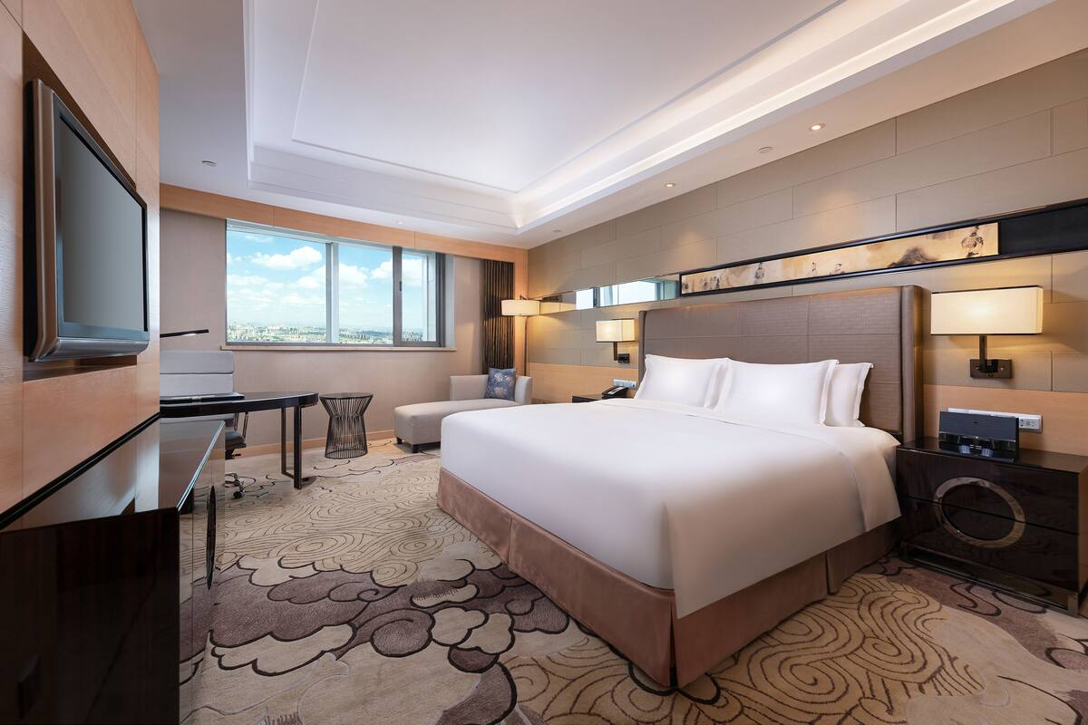 A modern hotel room with a large bed, a desk, a chair, and a TV.