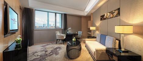 A modern hotel room with a large window, a sofa, a dining table, and a TV on the wall.