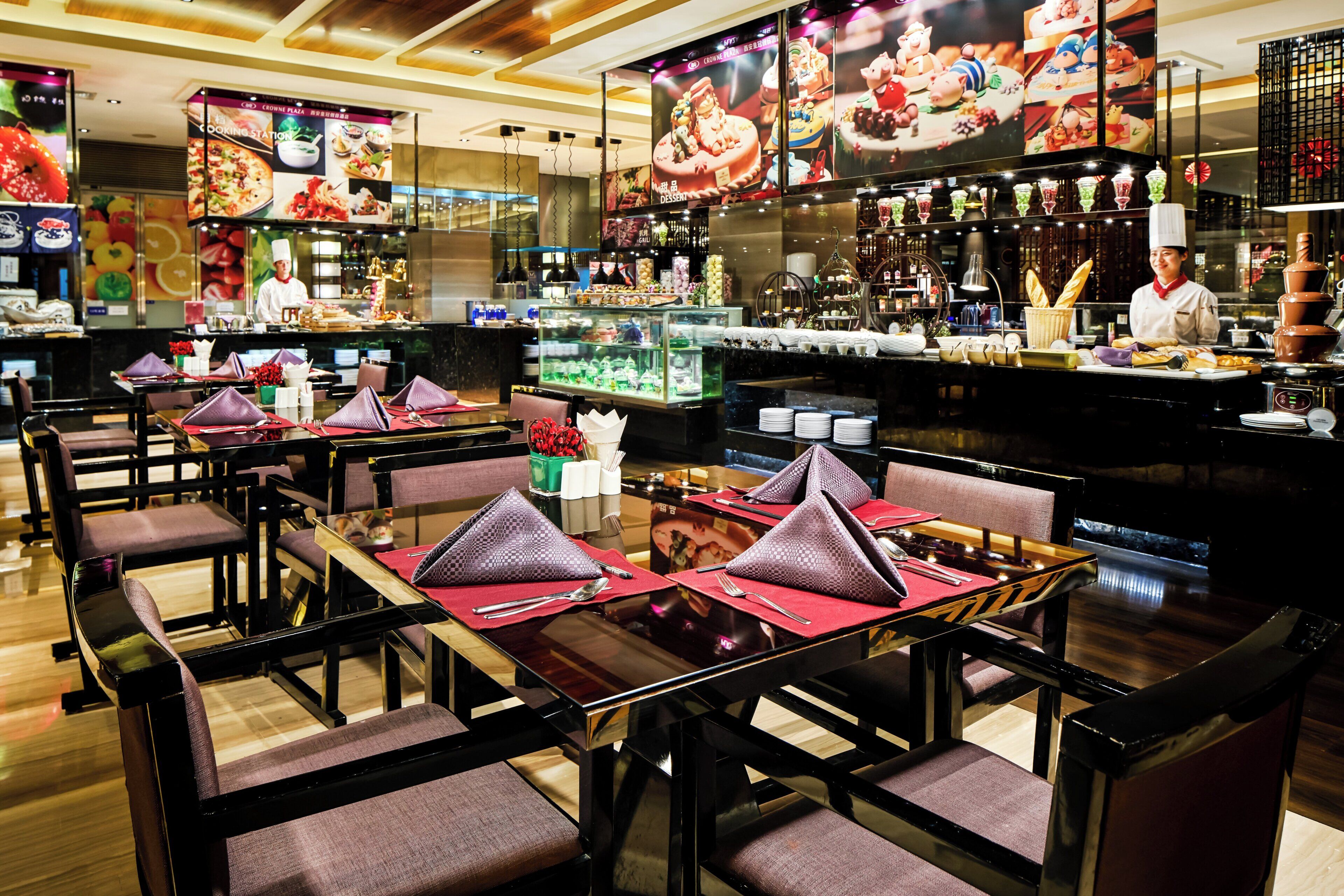 Un restaurante con mesas dispuestas para comer, una zona de bar con un bartender y una cocina al fondo.