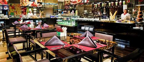 Un restaurante con mesas dispuestas para comer, una zona de bar con un bartender y una cocina al fondo.