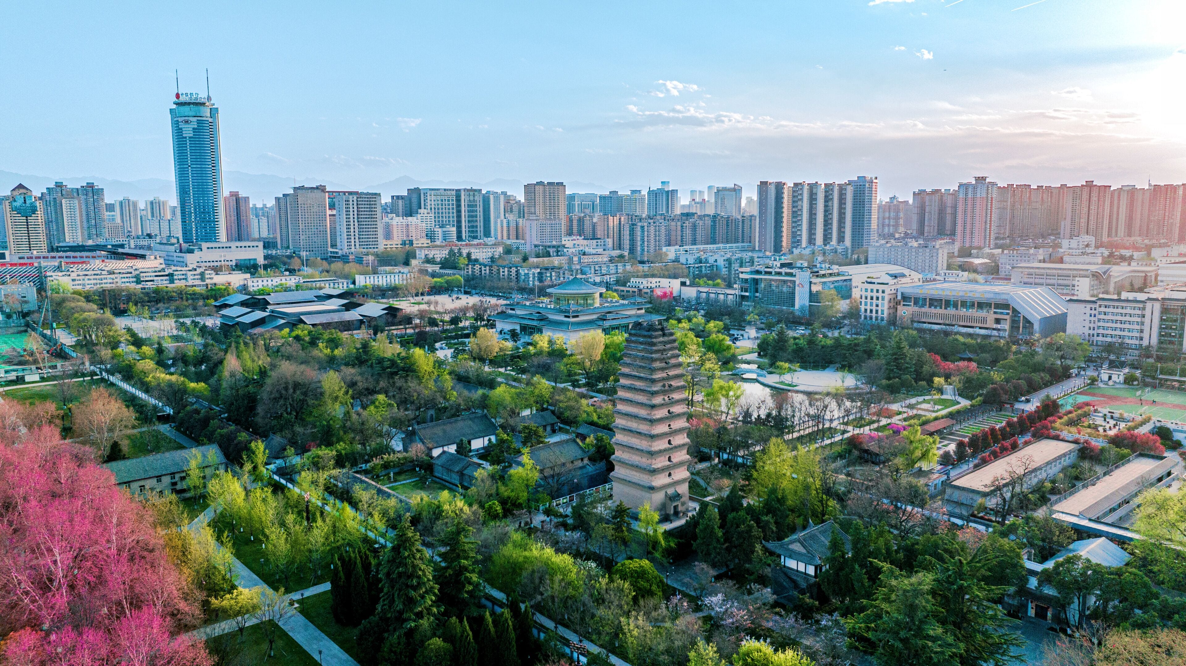 A cityscape with modern high-rise buildings, traditional pagoda, and surrounding greenery.