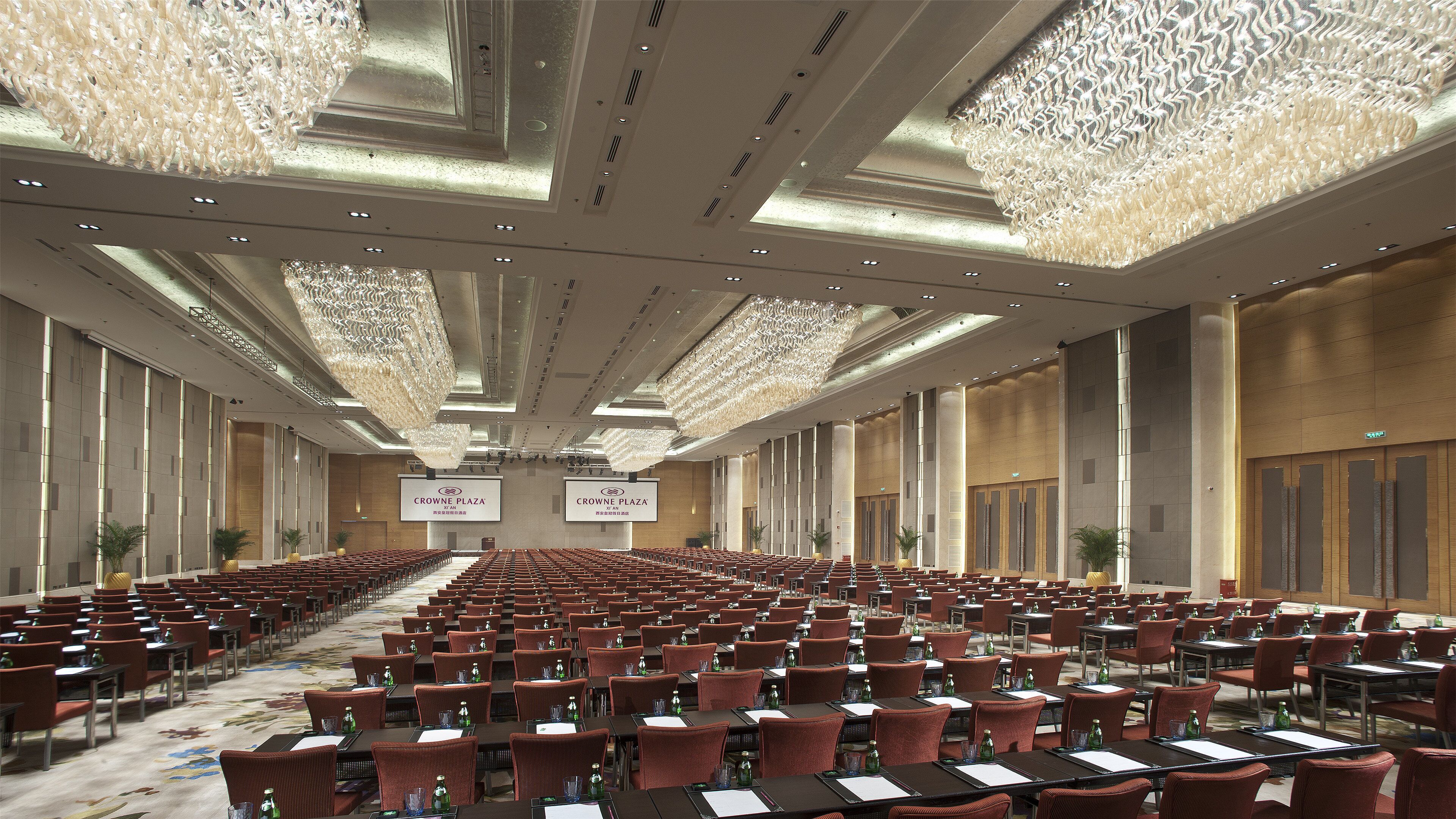 A spacious conference room with rows of tables and chairs, large chandeliers, and a high ceiling.
