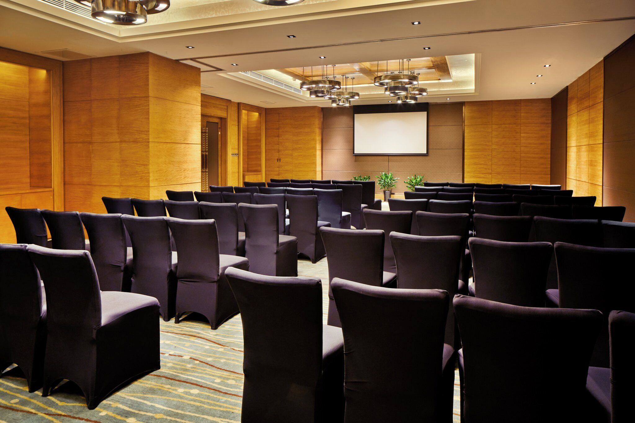 A conference room with rows of chairs, a projector screen, and a large window.