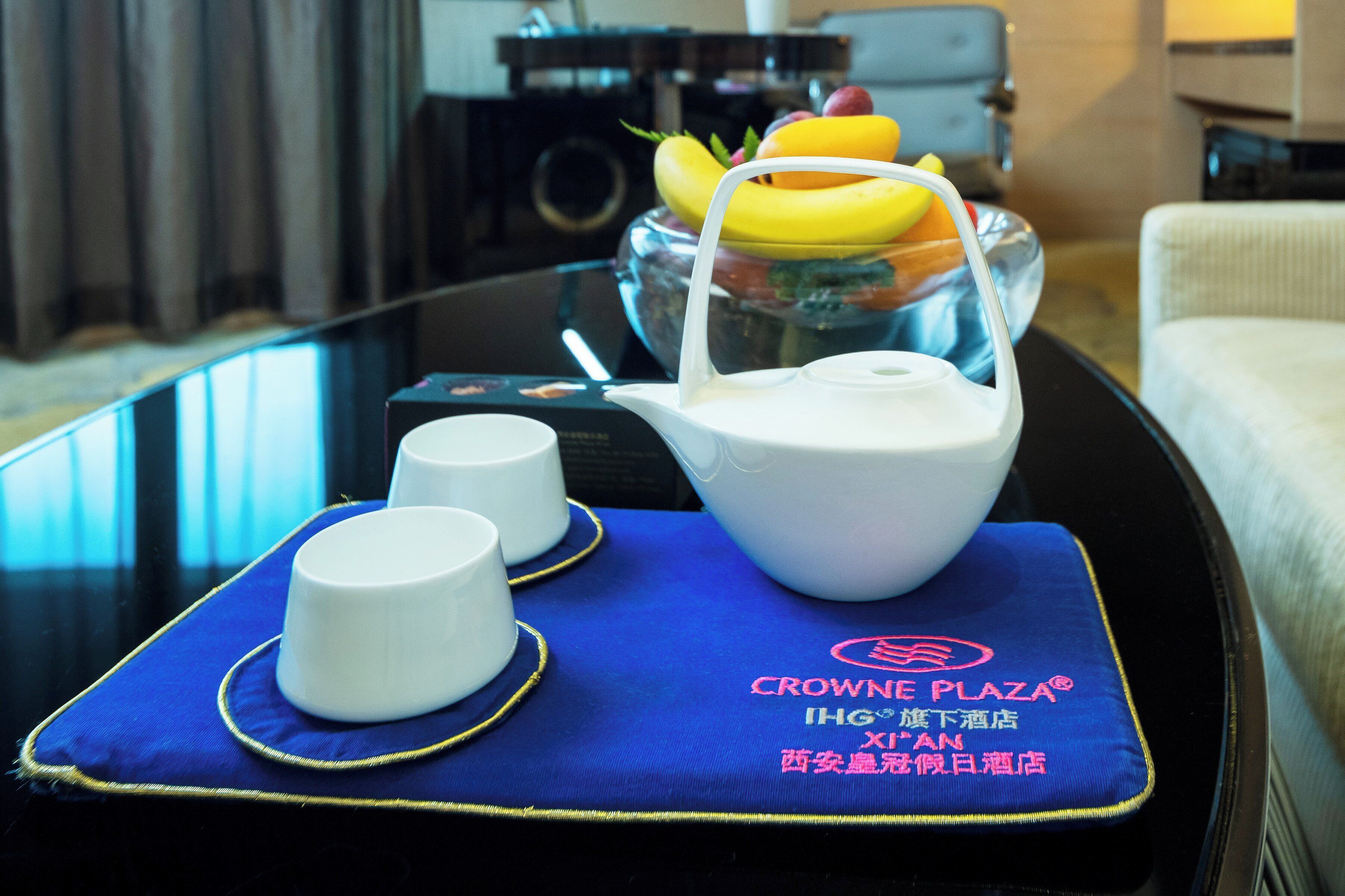 A hotel room with a glass table displaying a teapot, two cups, and a fruit bowl.