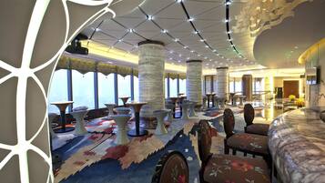 A hotel lobby with a modern design, featuring a patterned carpet, multiple seating areas, and a large window offering a view.