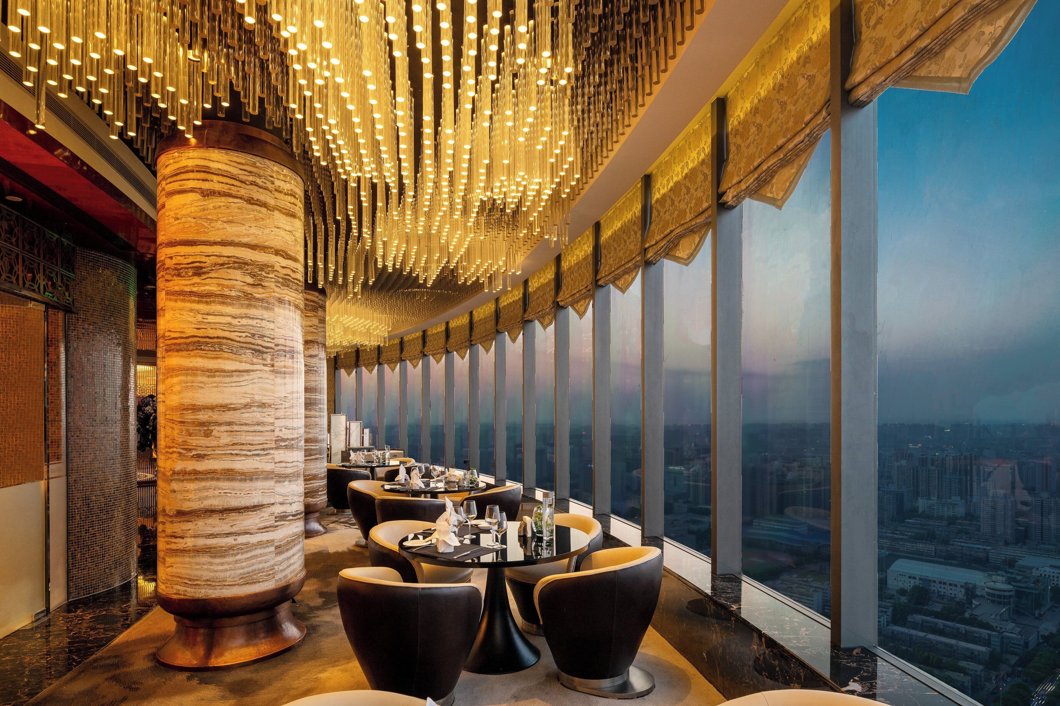 Un restaurante en un edificio alto con vistas panorámicas de la ciudad, decoración moderna y una lámpara de techo original.