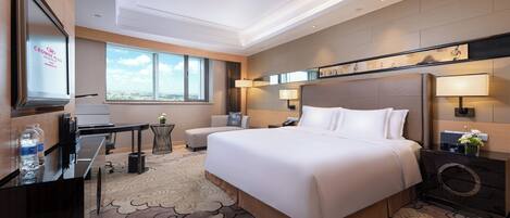 A hotel room with a large bed, a desk, a chair, a TV, and a view of the city.