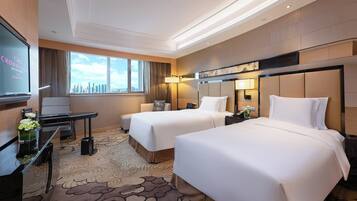 A hotel room with two beds, a desk, a TV, and a city view.