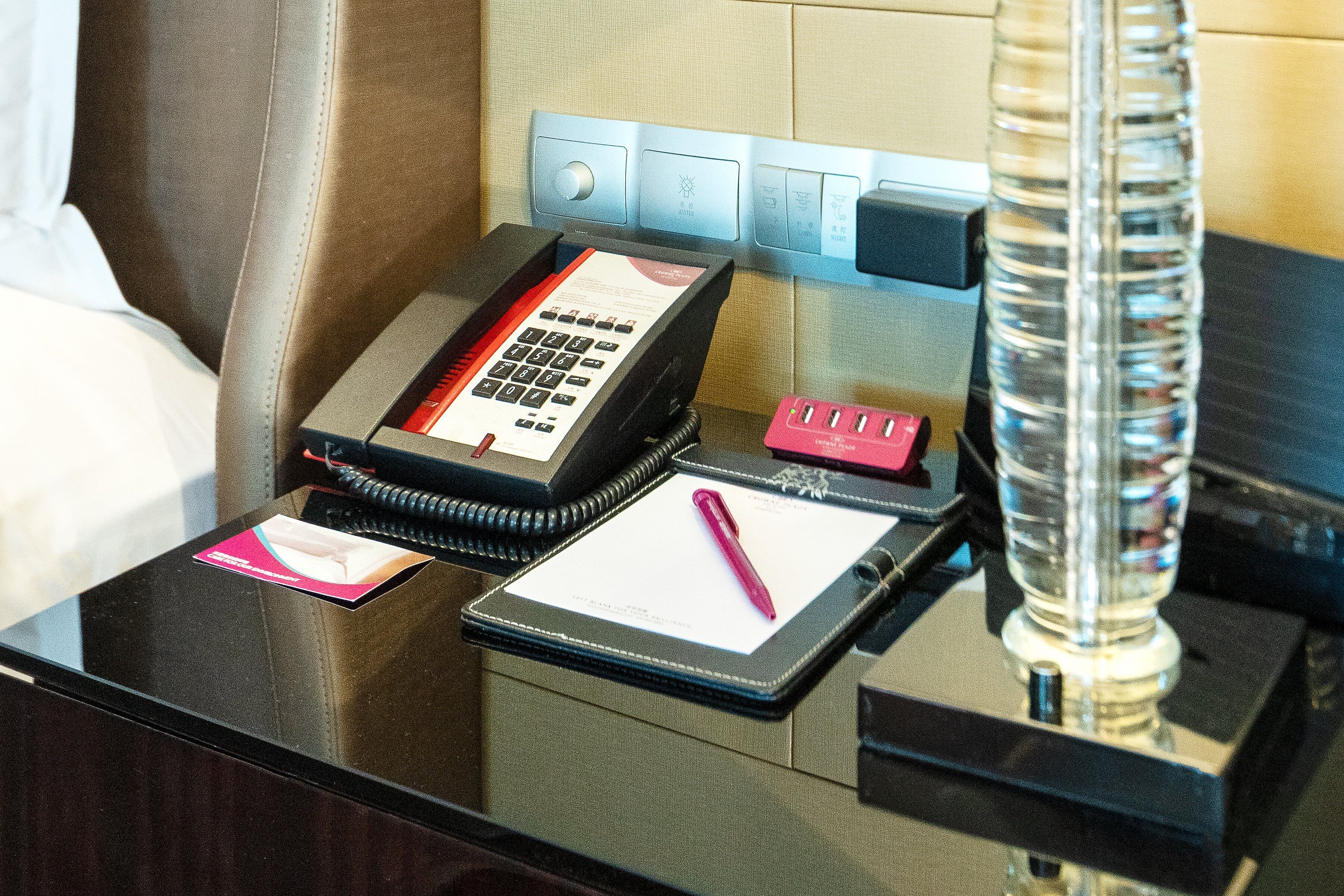 A hotel reception desk with a telephone, a notepad, a pen, and a lamp.
