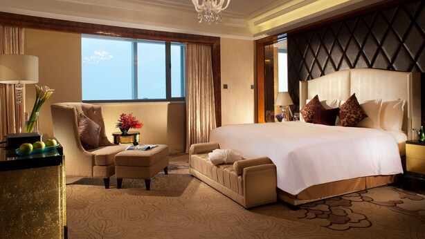 A spacious hotel room with a large bed, a sitting area with a sofa and armchair, a desk with a lamp, and a view of the sky through large windows. - Crowne Plaza Xian by IHG (Xi'an)