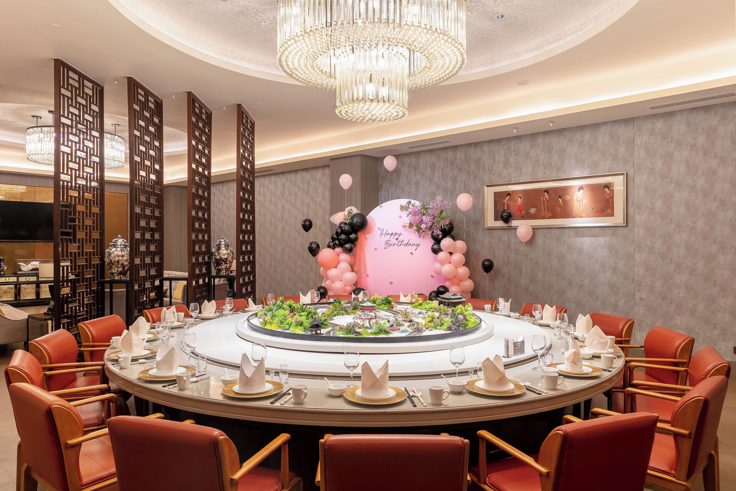 A round dining table with chairs, a chandelier, and a decorative cake centerpiece.