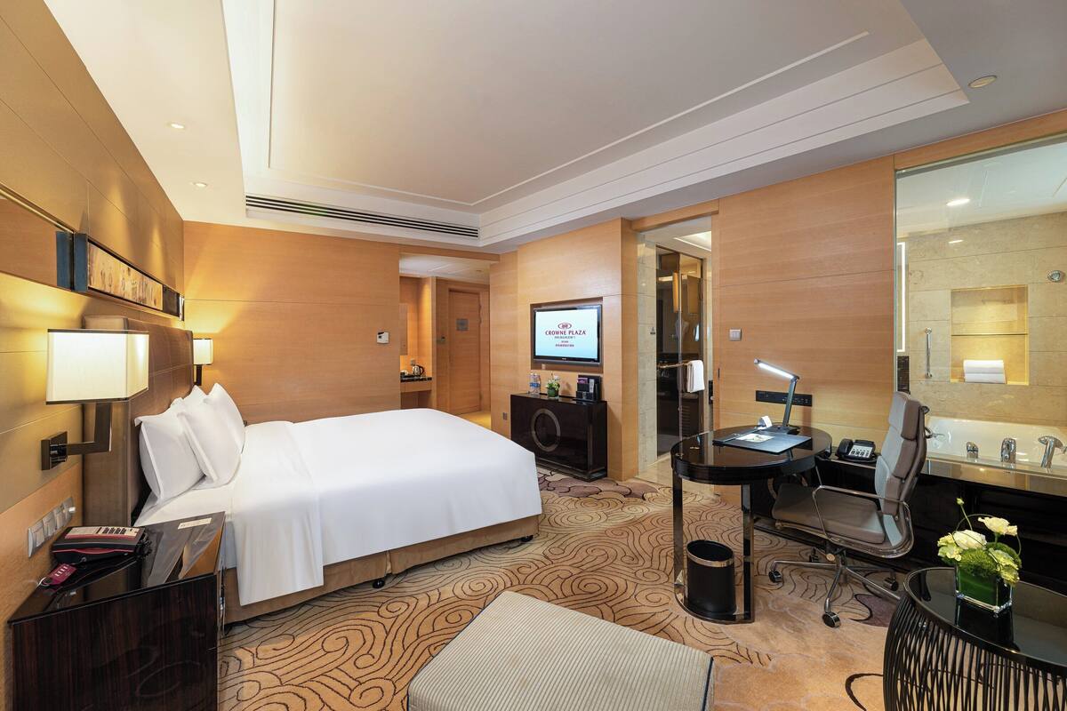 A hotel room with a bed, desk, chair, and a large mirror.