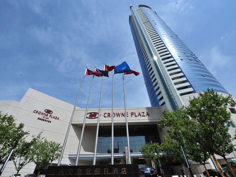 Un edificio moderno con el letrero 'CROWNE PLAZA' y varias banderas en mástiles.
