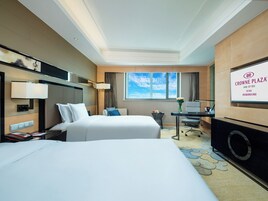 Habitación de hotel con dos camas, un escritorio, una silla, un televisor y una ventana con vistas al cielo.