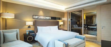 A hotel room with a large bed, two bedside tables, a chair, a sofa, a bathroom with a mirror, and a carpet with a leaf pattern.