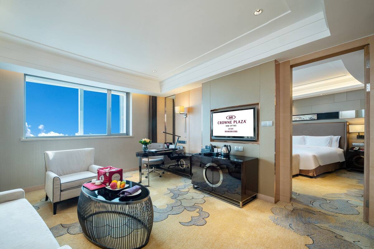 A hotel room with a bed, a desk, a chair, a sofa, and a television.