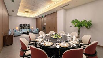 A conference room with a round table set for a meeting, surrounded by chairs, and a large plant in the corner.